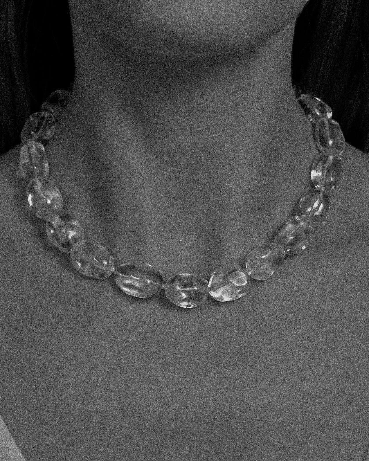 Clear beaded necklace worn by a person against a neutral background